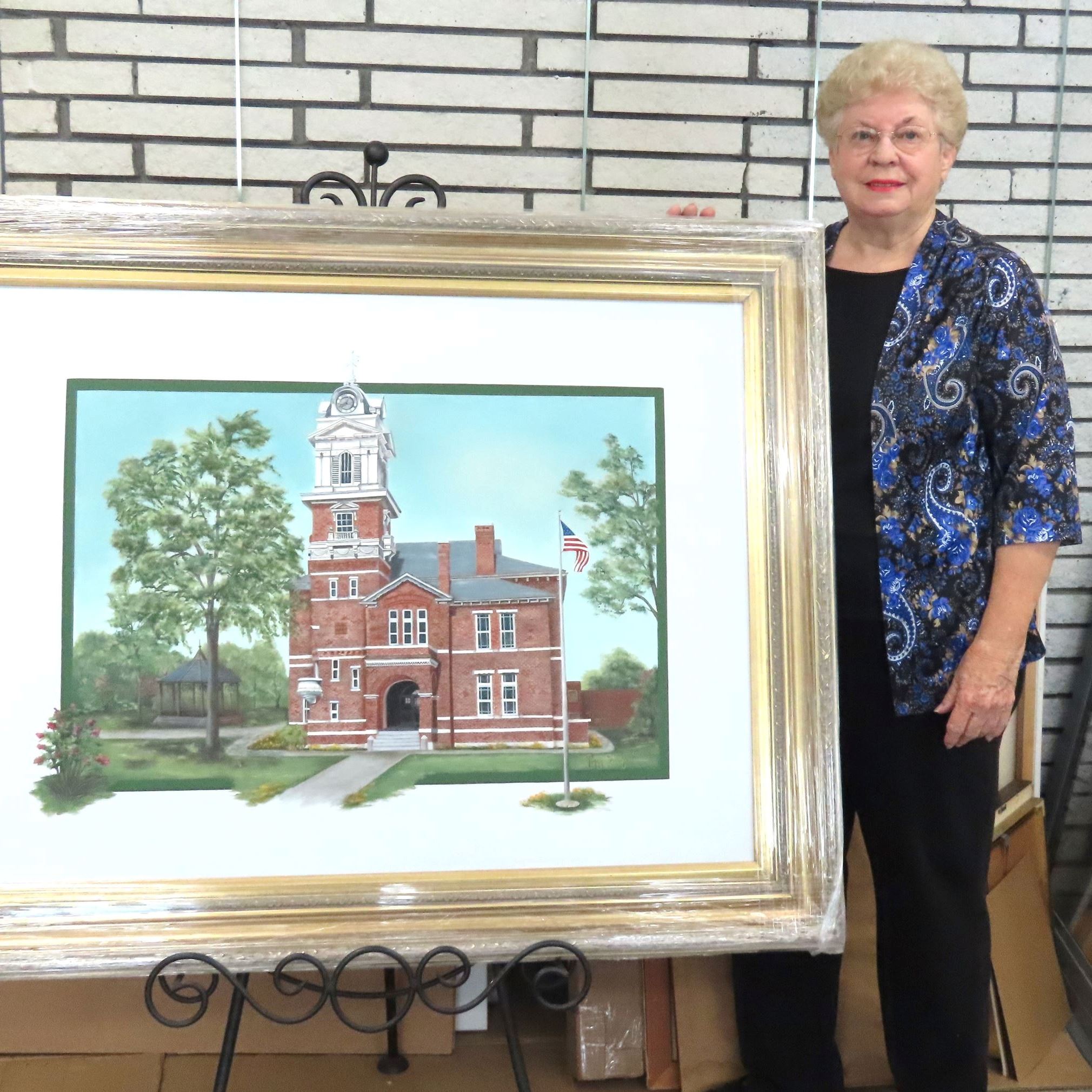 older woman with glasses standing next to painting on easel, height reaches her shoulder