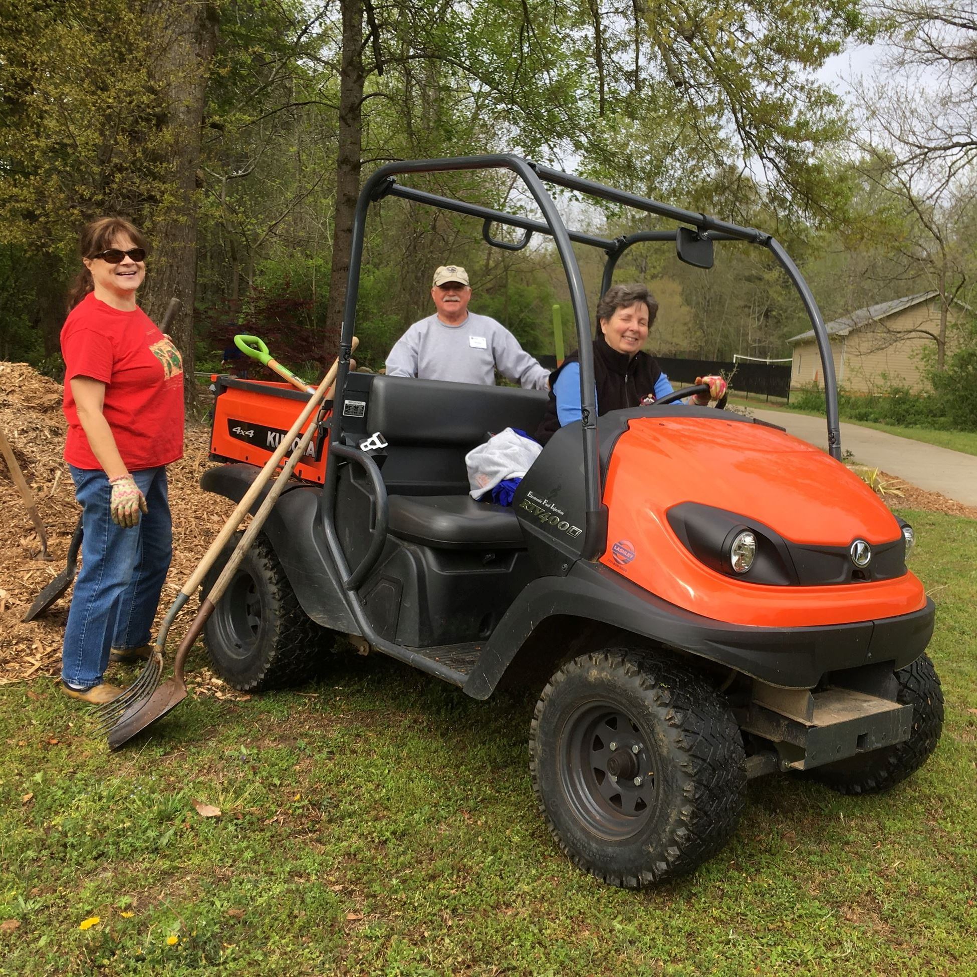 a male and two female gardeners pose with shovels, mulch and a Kubota UTV