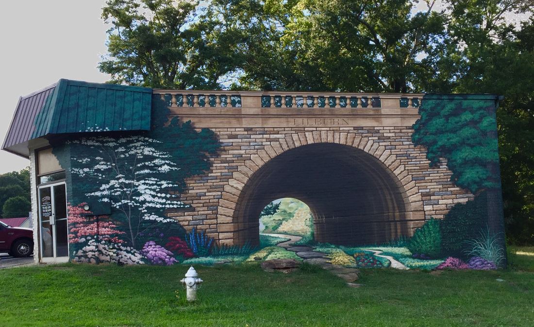 painted mural on a brick building of trees and flowers under a bridge (tunnel)