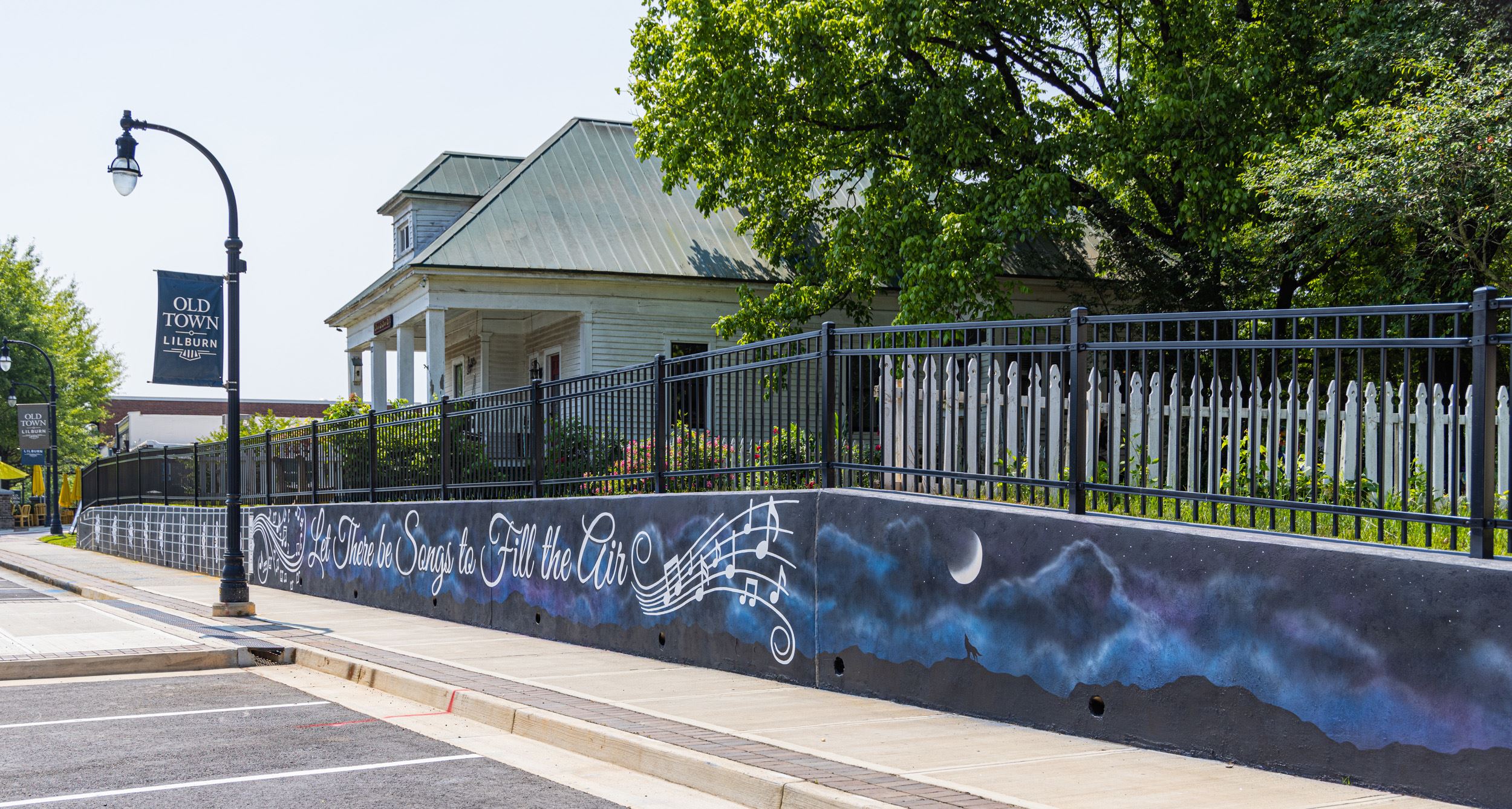 painted mural on a retaining wall by a sidewalk of music notes & a wolf howling at moon on night sky