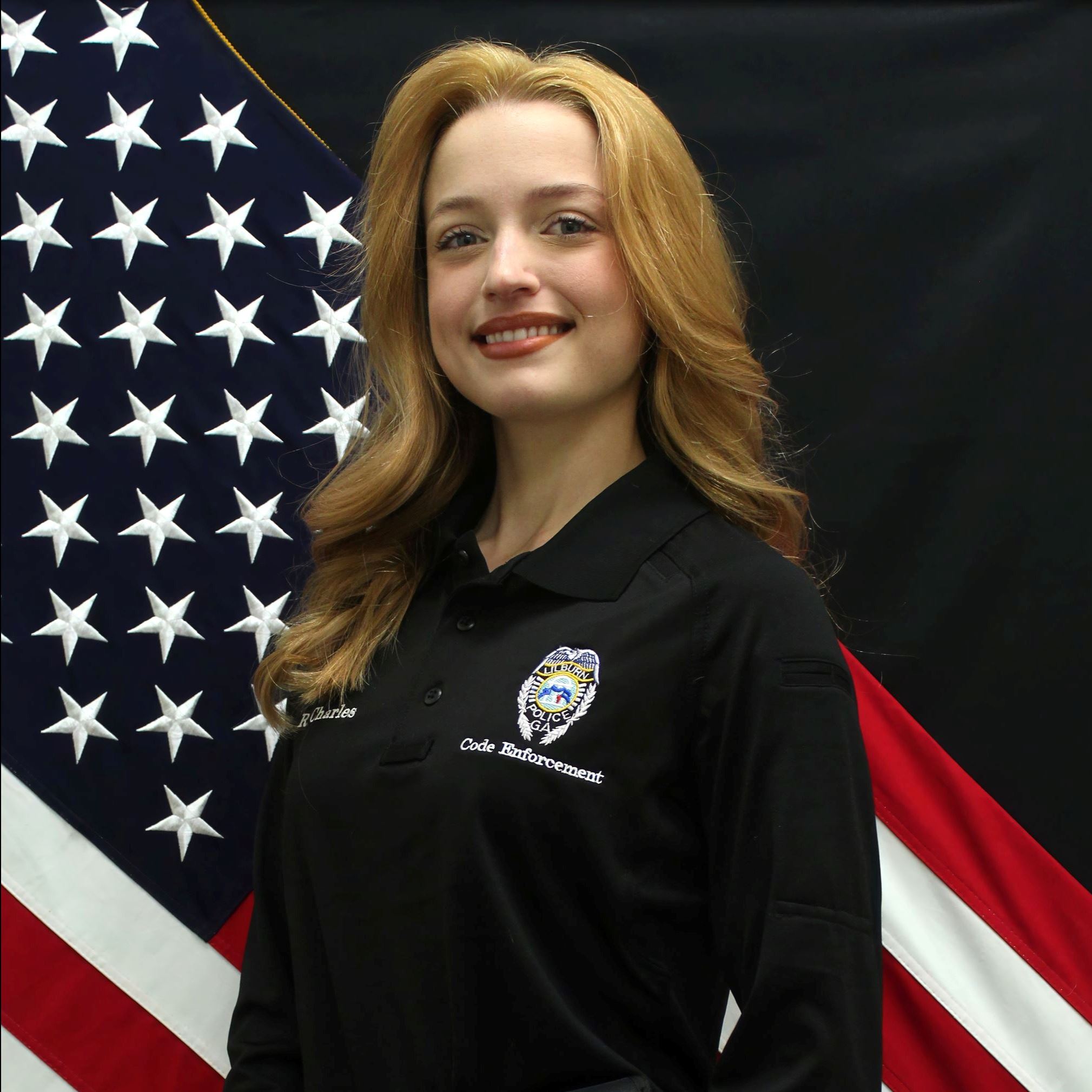 Headshot of Rachel Charles female with long red hair wearing black polo and khakis
