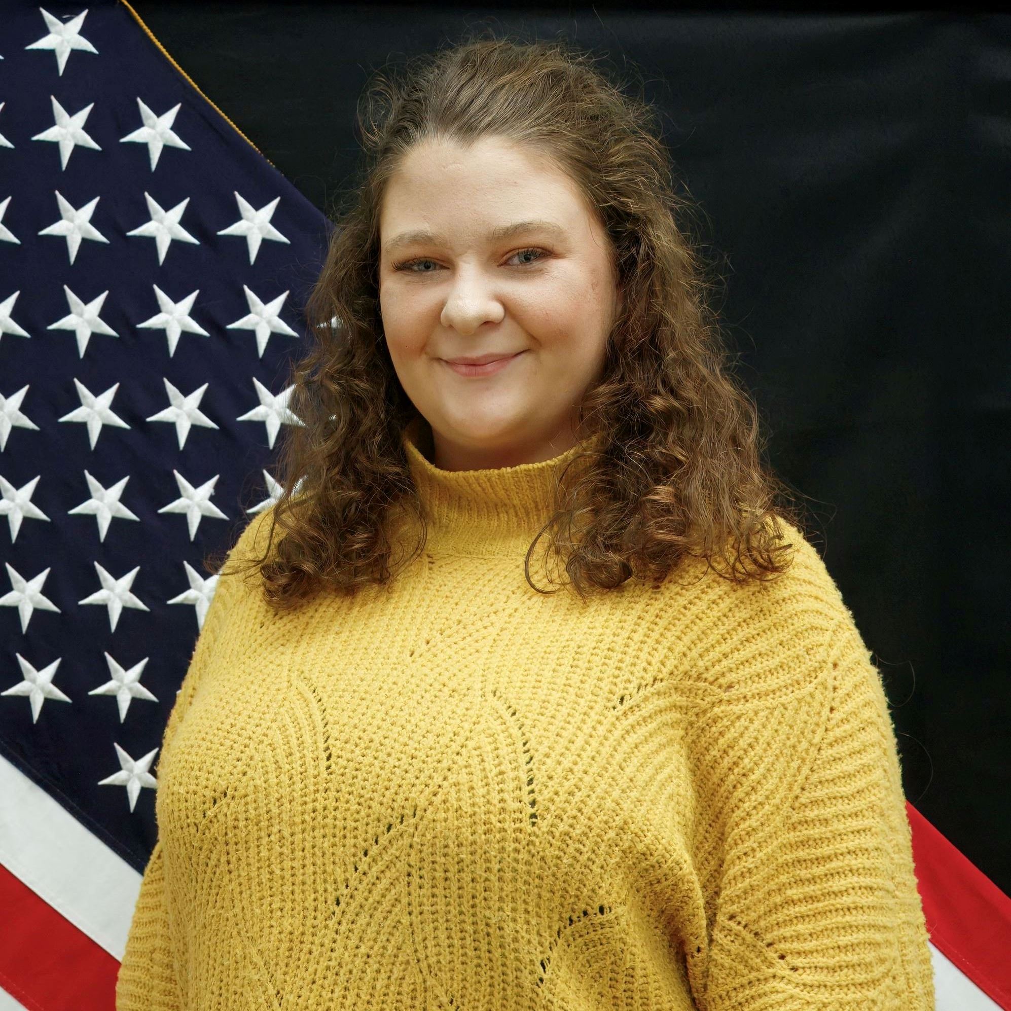 Headshot of Payton Deweese female with long curly dark hair wearing yellow sweater