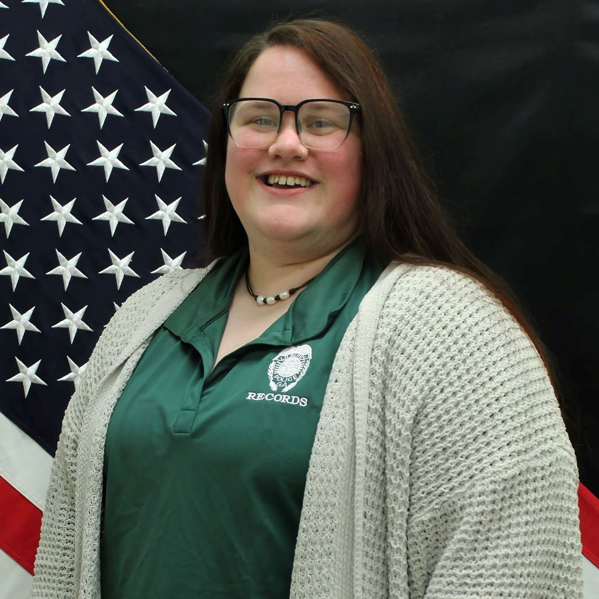 Headshot of Ashley Stainbrook feale with short dark hair and glasses wearing dark green polo 