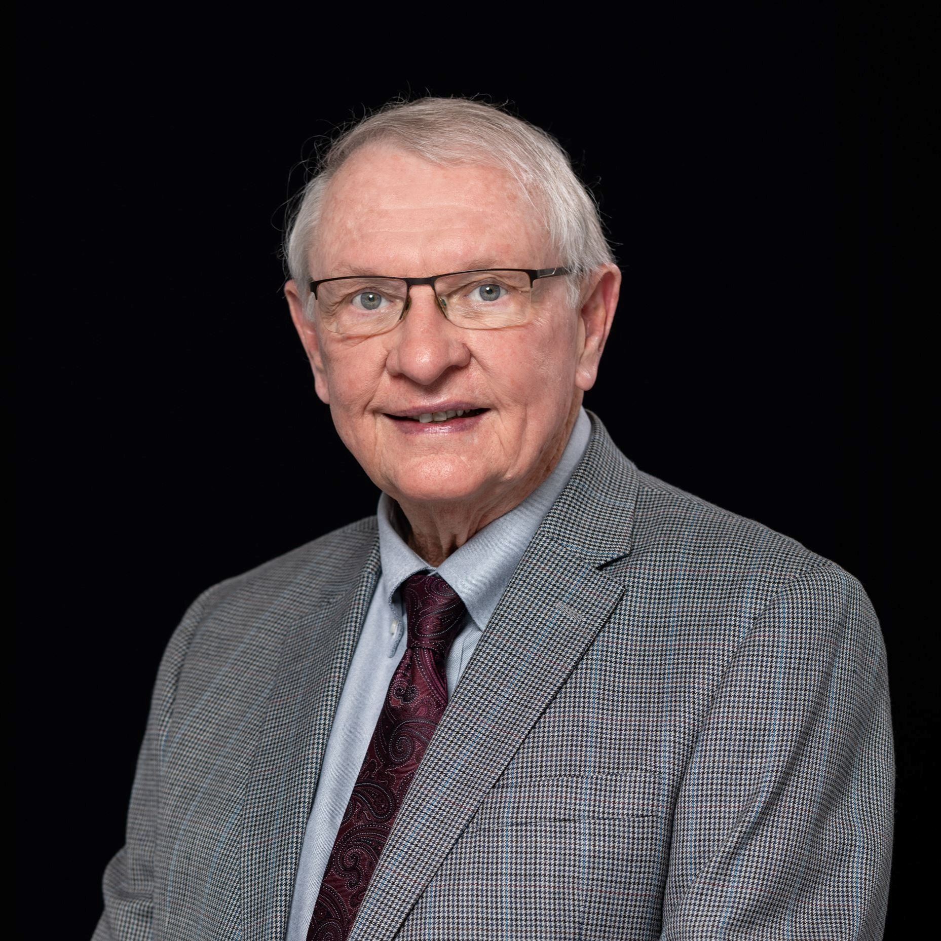 Headshot of Emil Powella male with white hair and glasses in gray suit
